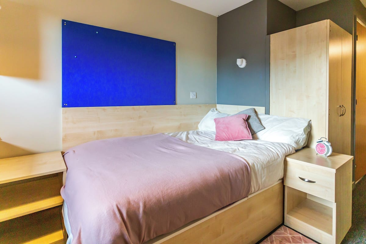 A modern bedroom with a bed, a nightstand, a wardrobe, and a blue wall.