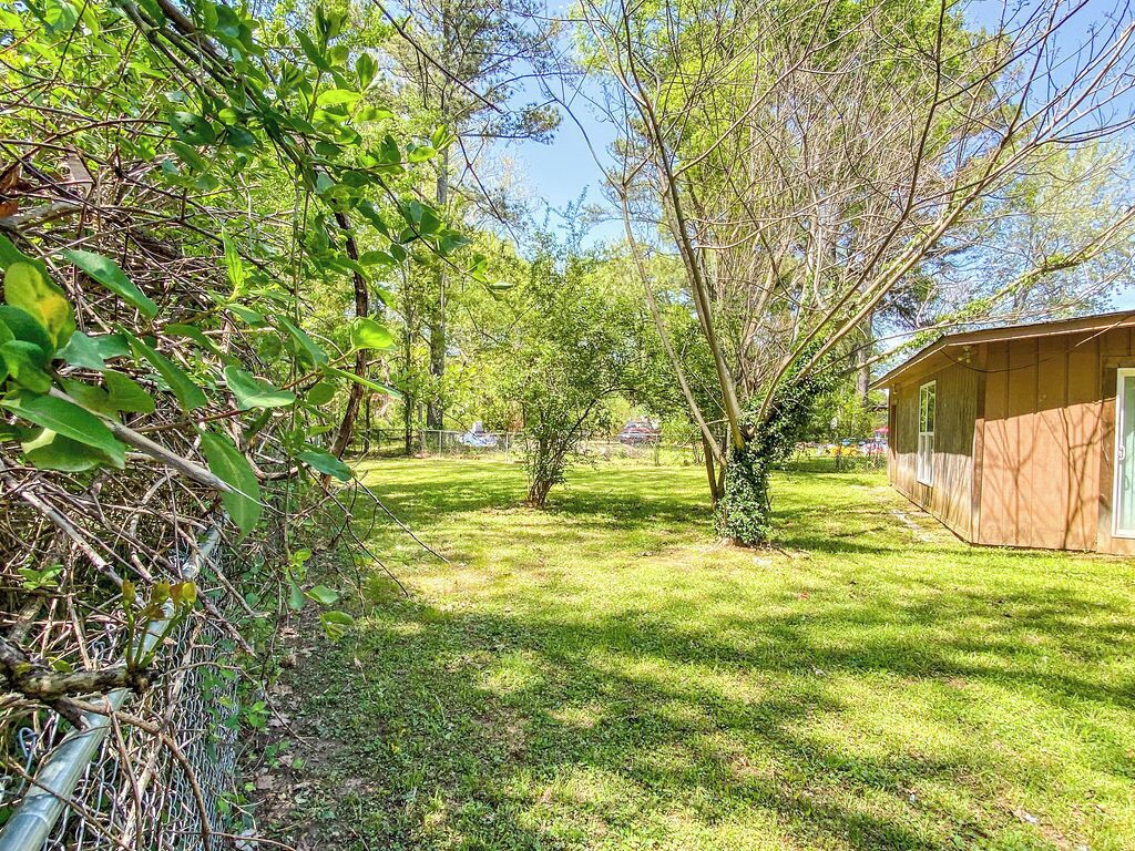 A wooden cabin with a fenced yard, surrounded by trees and greenery.