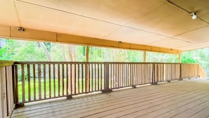 Eine offene Holzterrasse mit Geländer, unter einem überdachten Bereich mit Blick auf Grünflächen.