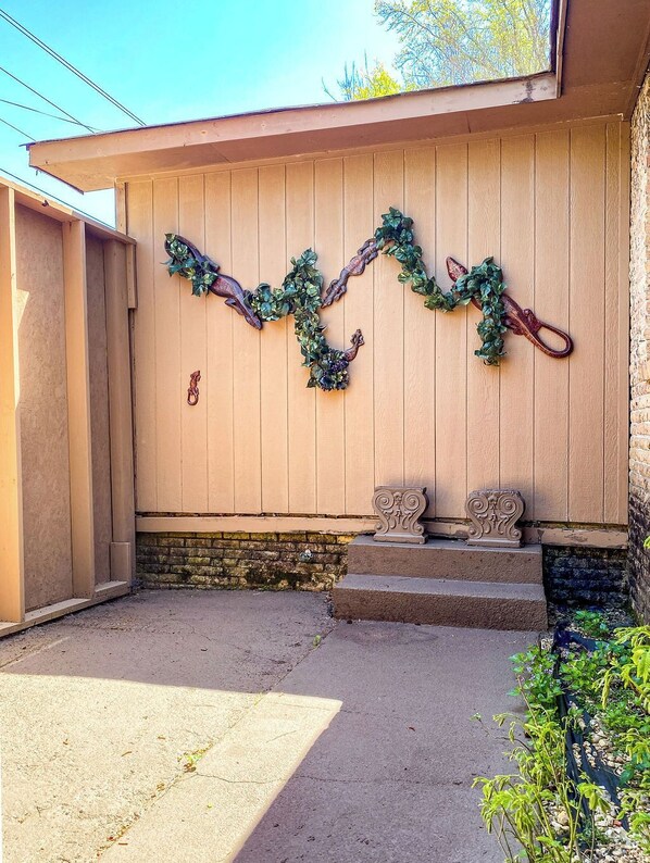 A building exterior with a wooden wall, a metal gate, and a small garden area with steps leading up to the entrance. - The Blue Spring Oasis (Huntsville)