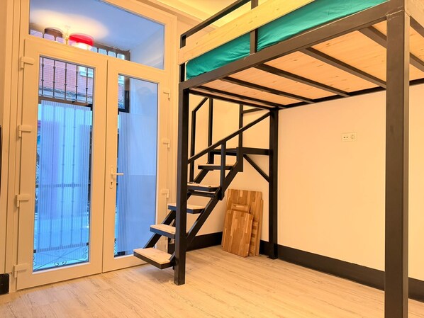 Une pièce avec un lit superposé, un escalier et une porte à panneaux de verre.