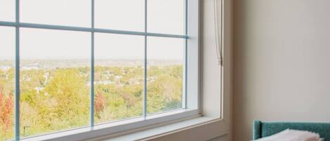 A room with a large window offering a view of a cityscape and trees.