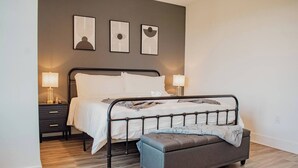 Een slaapkamer met een metalen bedframe, een nachtkastje met een lamp en een bankje.