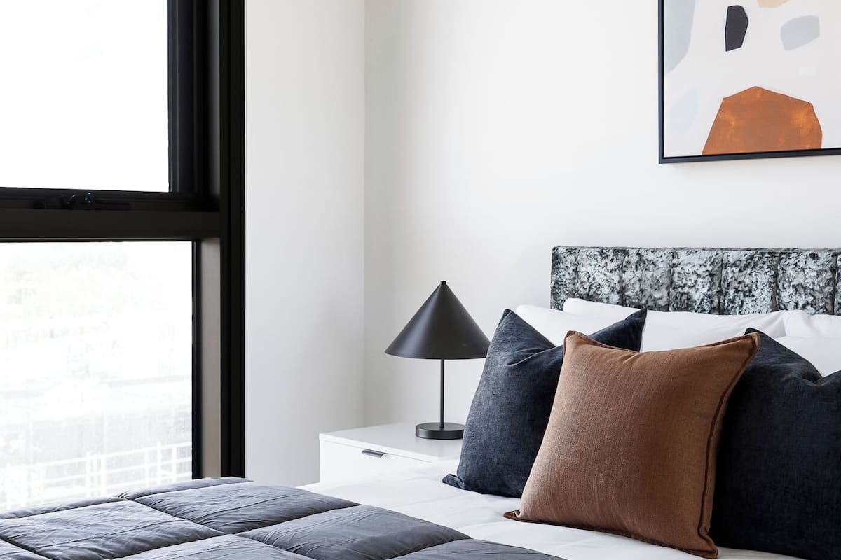 A modern bedroom with a large bed, a nightstand, a lamp, and a window.