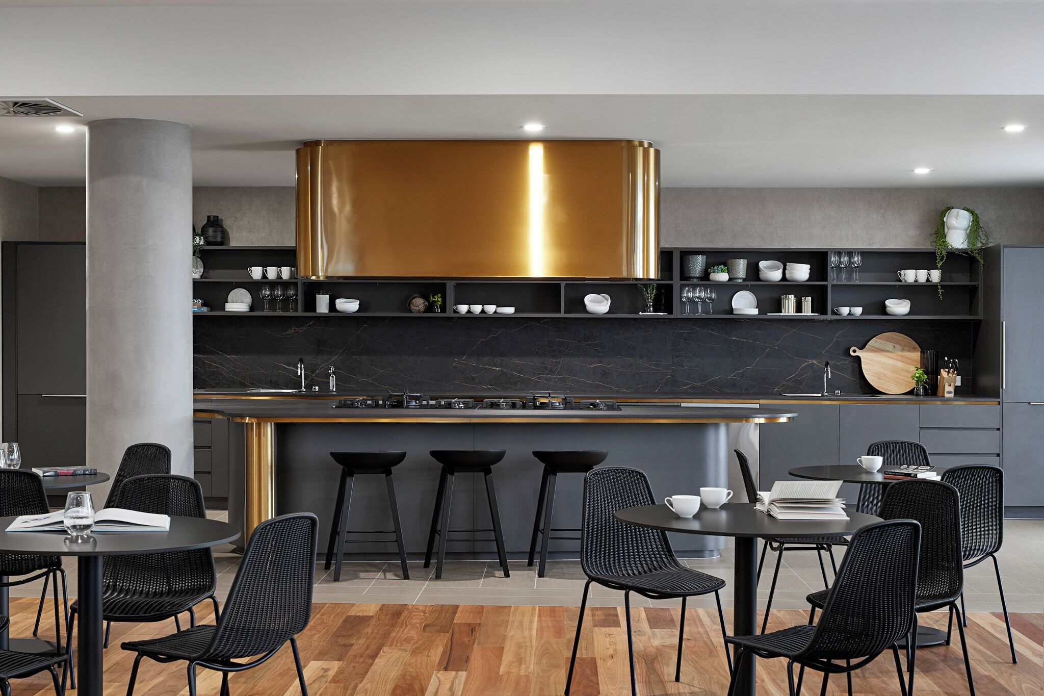 Une cuisine moderne dotée d’un îlot central, de tabourets de bar noirs et d’un coin repas avec des tables et des chaises rondes.