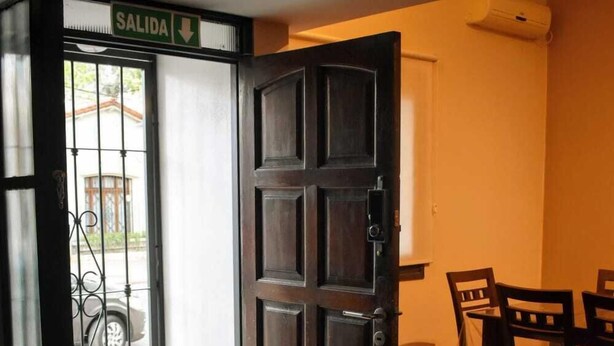 A wooden door with a sign reading "SALIDA" (exit), a dining area with chairs and a table, and a wooden floor. - Cosmo Mendoza Suites (Mendoza)