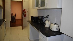 A compact kitchen with a microwave, coffee maker, and toaster on the counter, a stove, and cabinets with glass doors. - Cosmo Mendoza Suites (Mendoza)