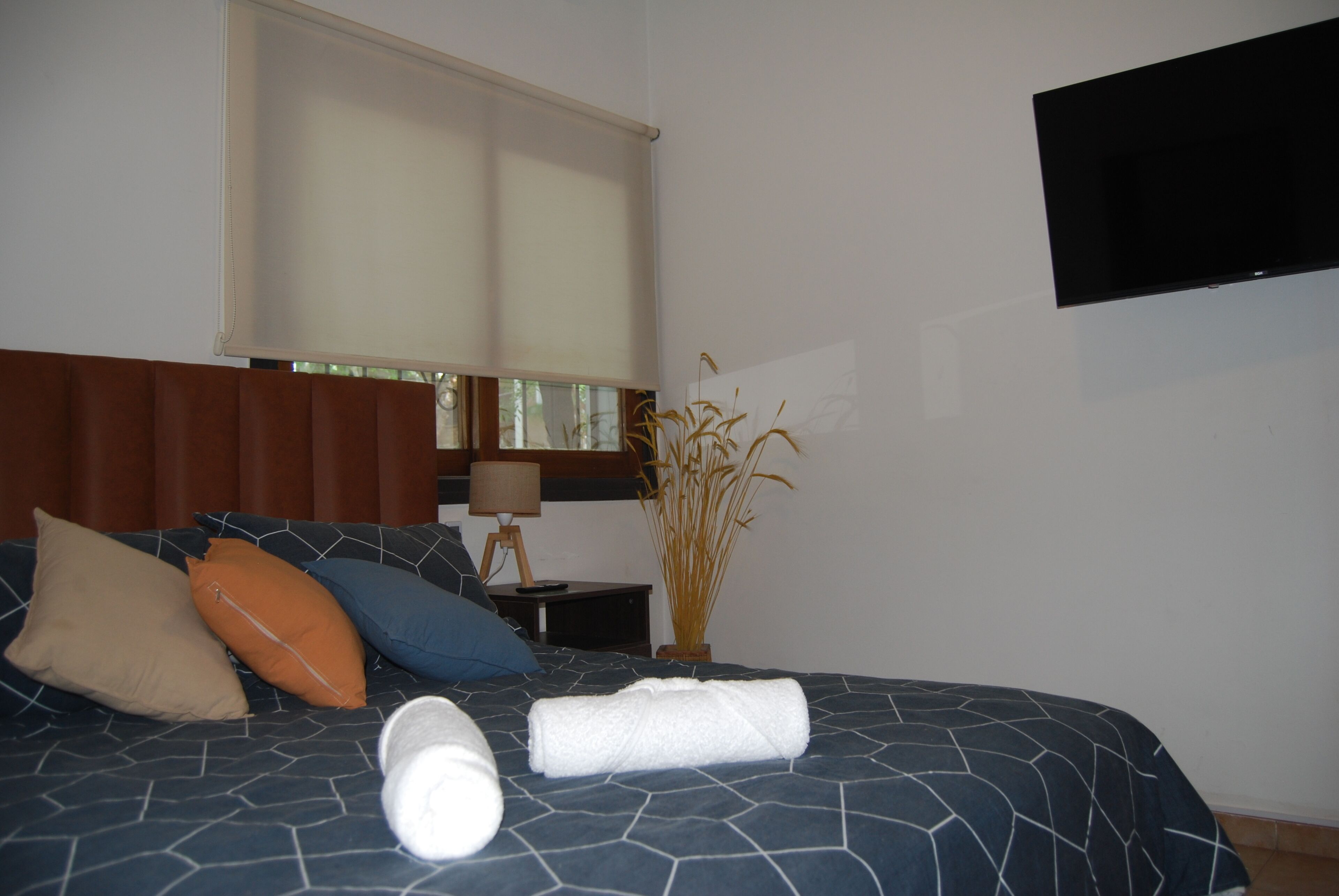 A neatly made bed with a patterned bedspread, a rolled white towel, and several pillows.