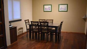 Een eetruimte met een houten tafel en stoelen, twee ingelijste foto’s aan de muur en een raam met jaloezieën.