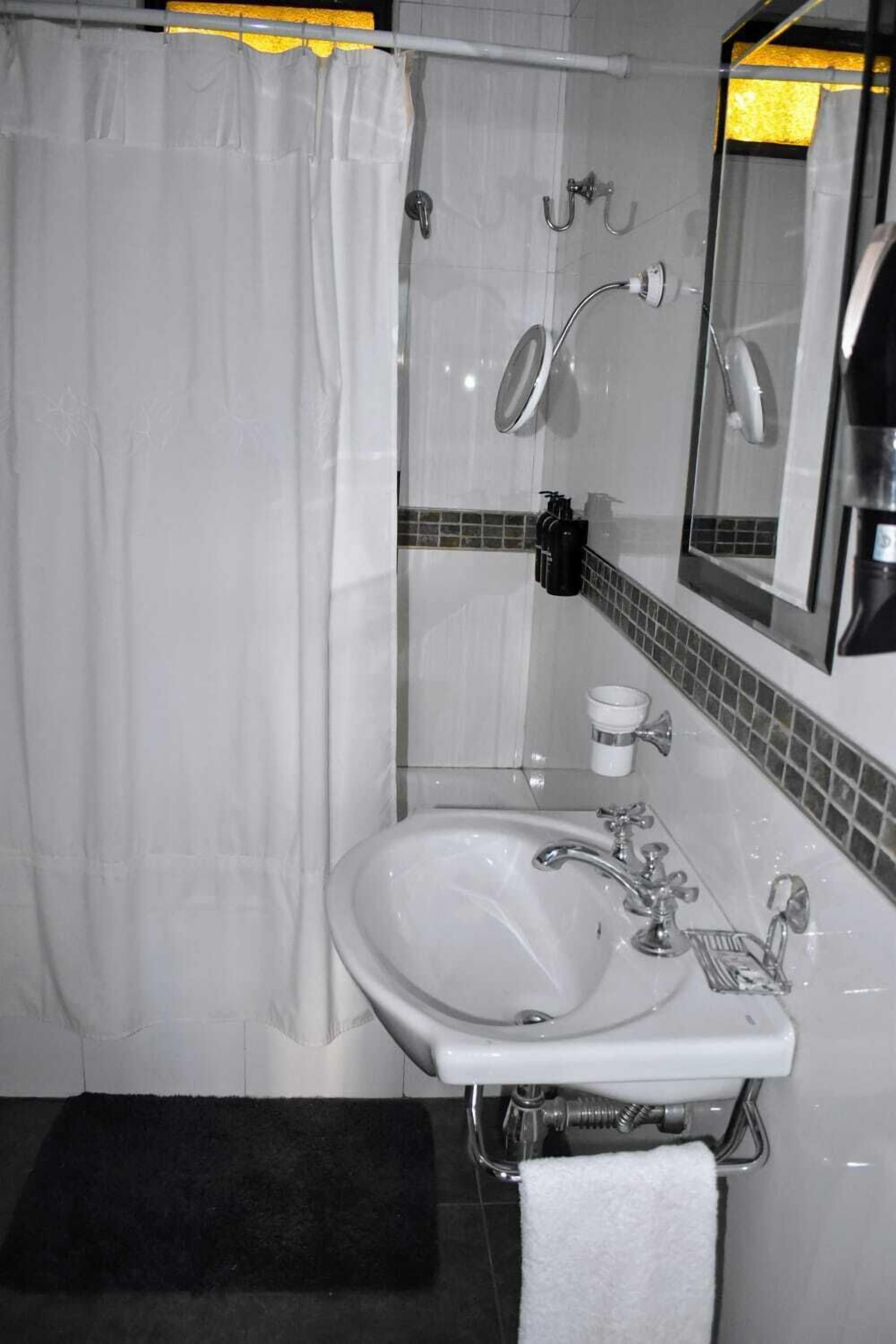 A bathroom with a white sink, a mirror, a shower curtain, and a towel rack.