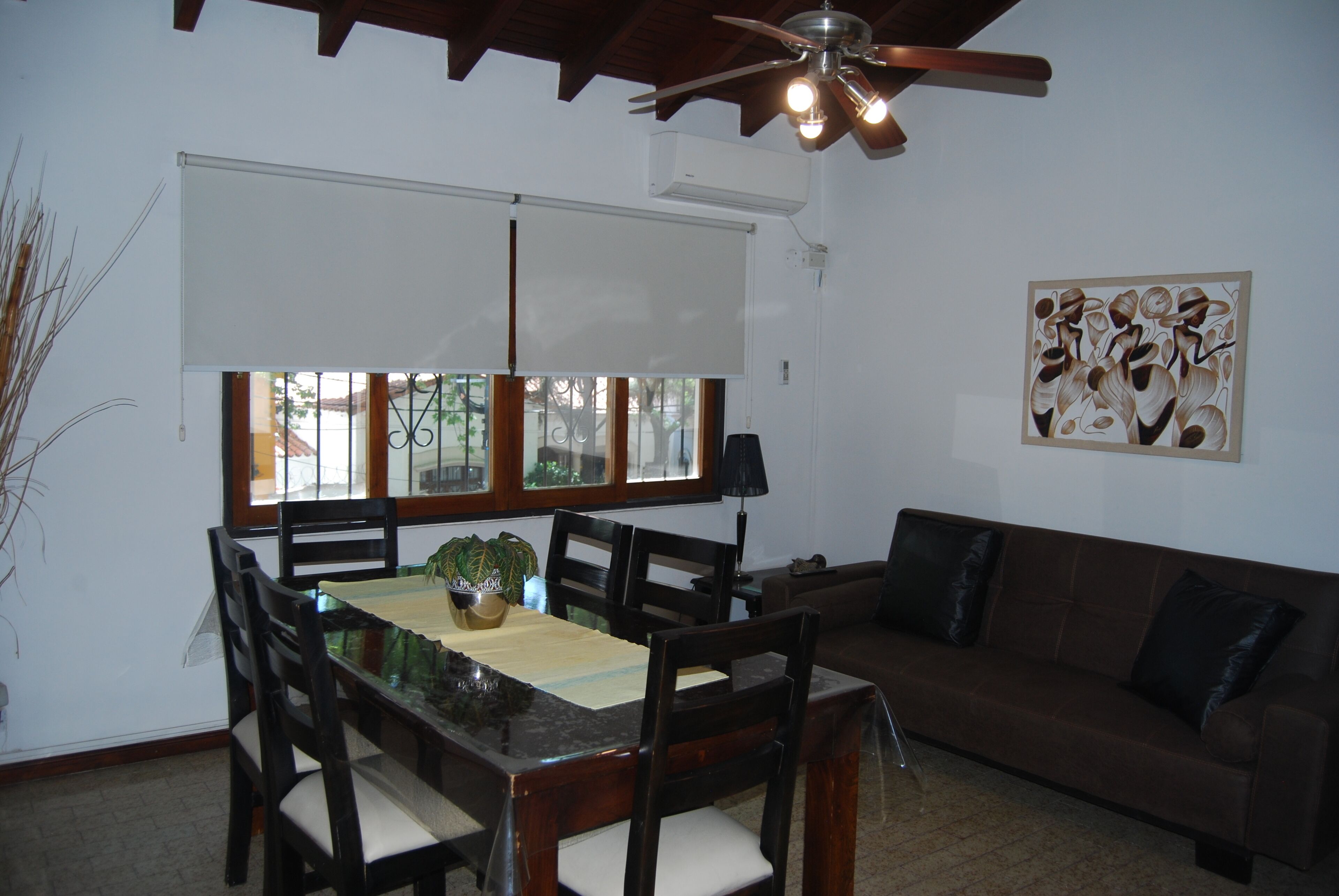 Uma área de refeições com mesa, cadeiras, ventilador de teto e janela com persianas.