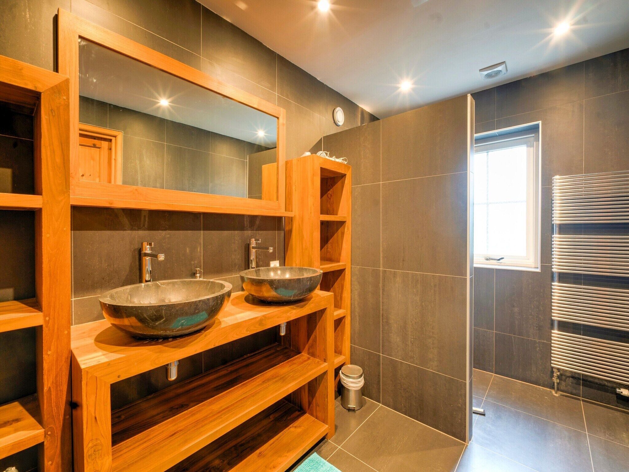 Un baño moderno con dos lavamanos grandes, estantes de madera, un espejo y un perchero para toallas.