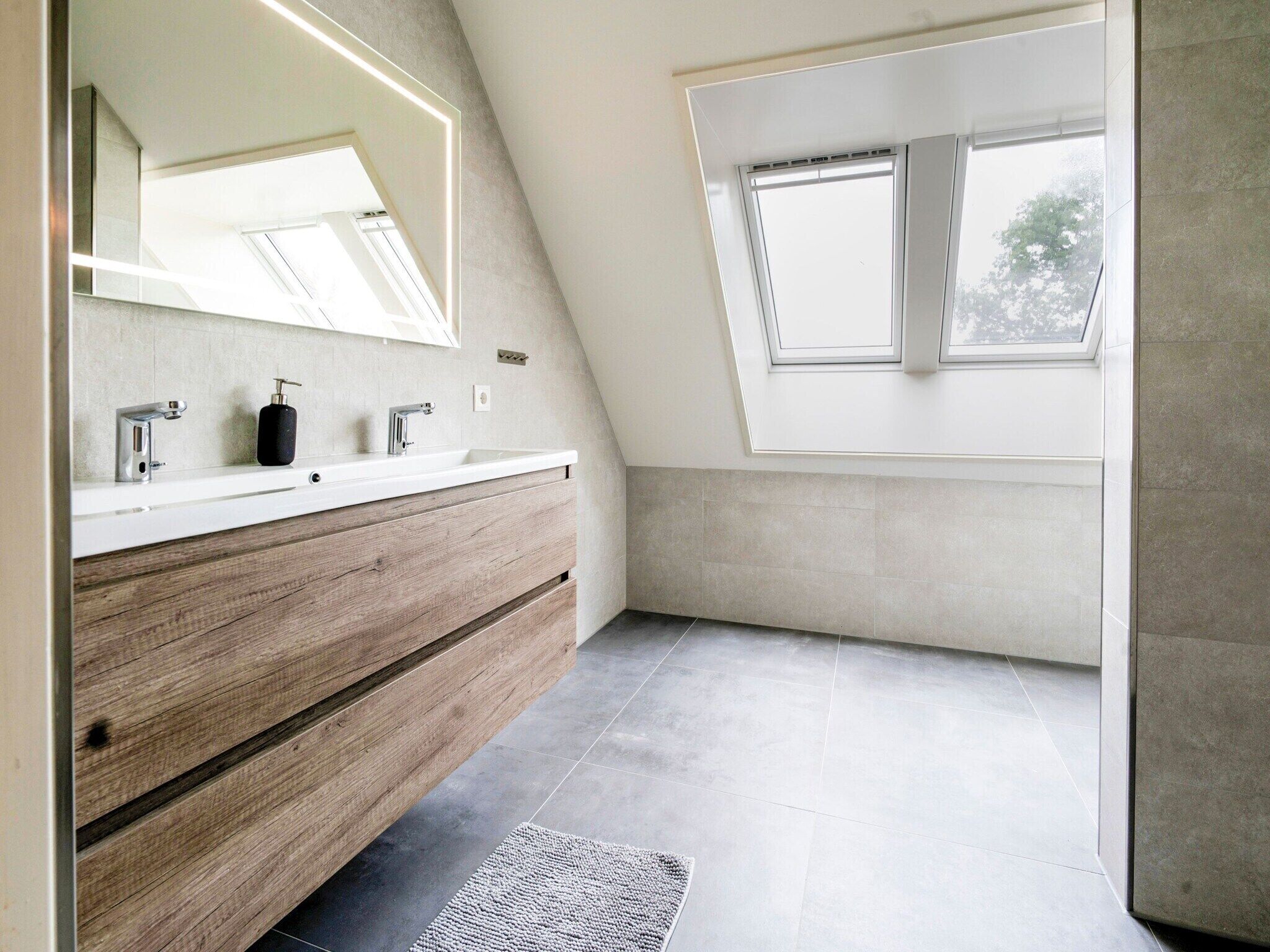 Une salle de bain moderne avec un plafond en pente, un puits de lumière, un meuble-lavabo en bois et un grand miroir.