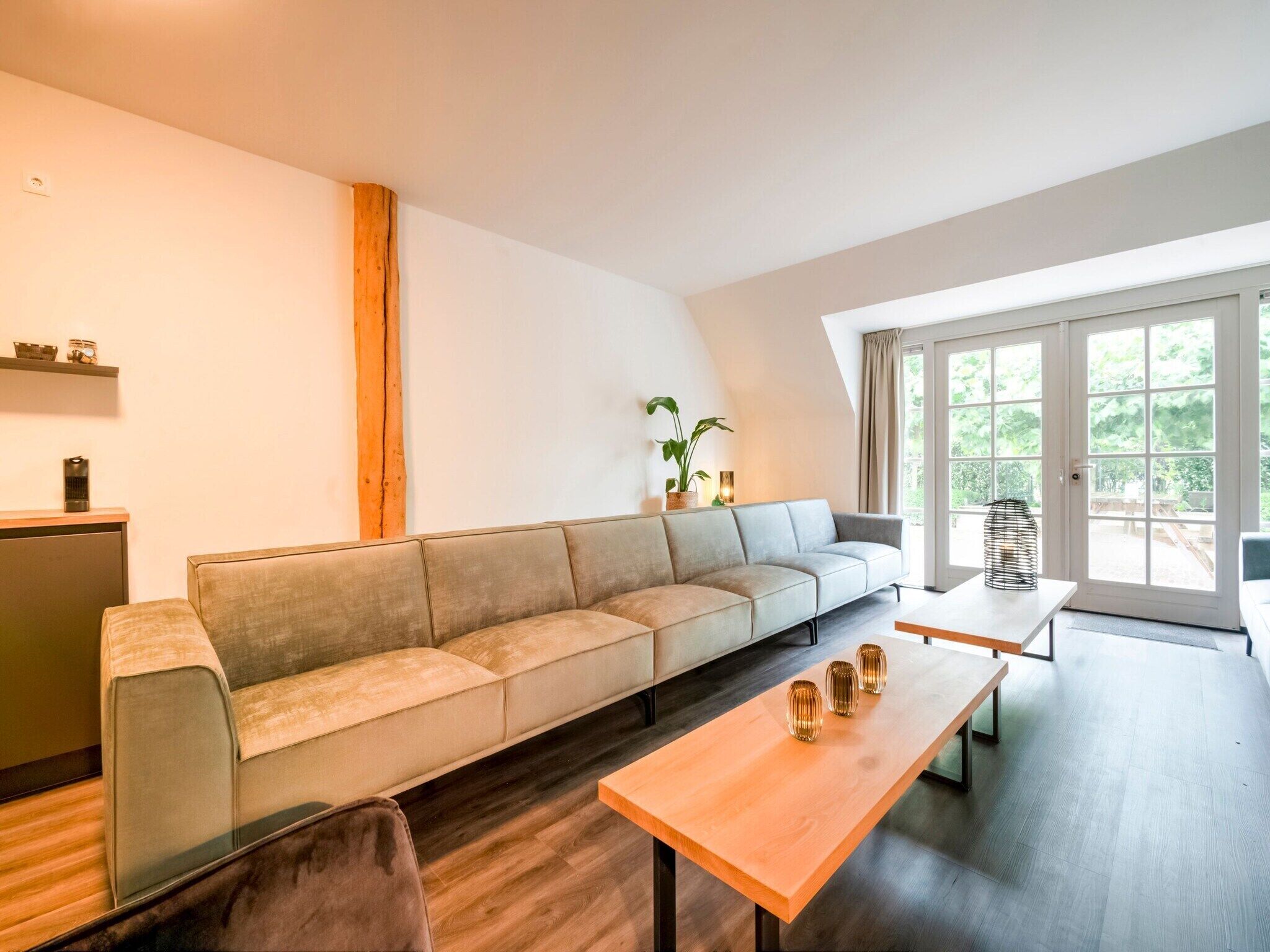Ein modernes Wohnzimmer mit einer Couch, einem Holztisch und einem großen Fenster mit Blick auf Grünflächen.