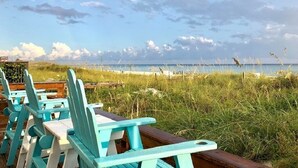 Een zitgedeelte aan het strand met turquoise stoelen en een houten tafel.