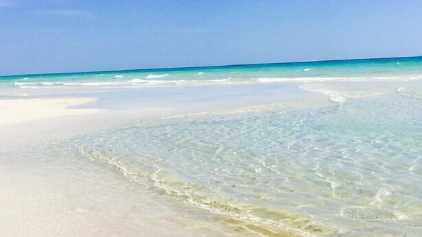 Een strand met helder turquoise water en wit zand.