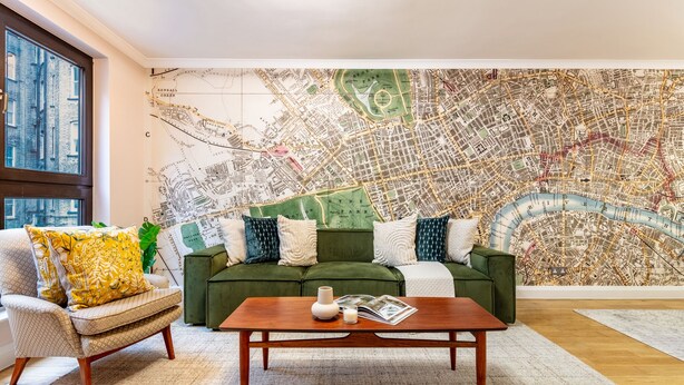 A living room with a green sofa, a wooden coffee table, and a large map mural on the wall. - Spacious 2BR House by Madame Tussauds  (London)