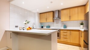 A modern kitchen with white cabinetry, a central island, and a stainless steel range hood. - Spacious 2BR House by Madame Tussauds  (London)