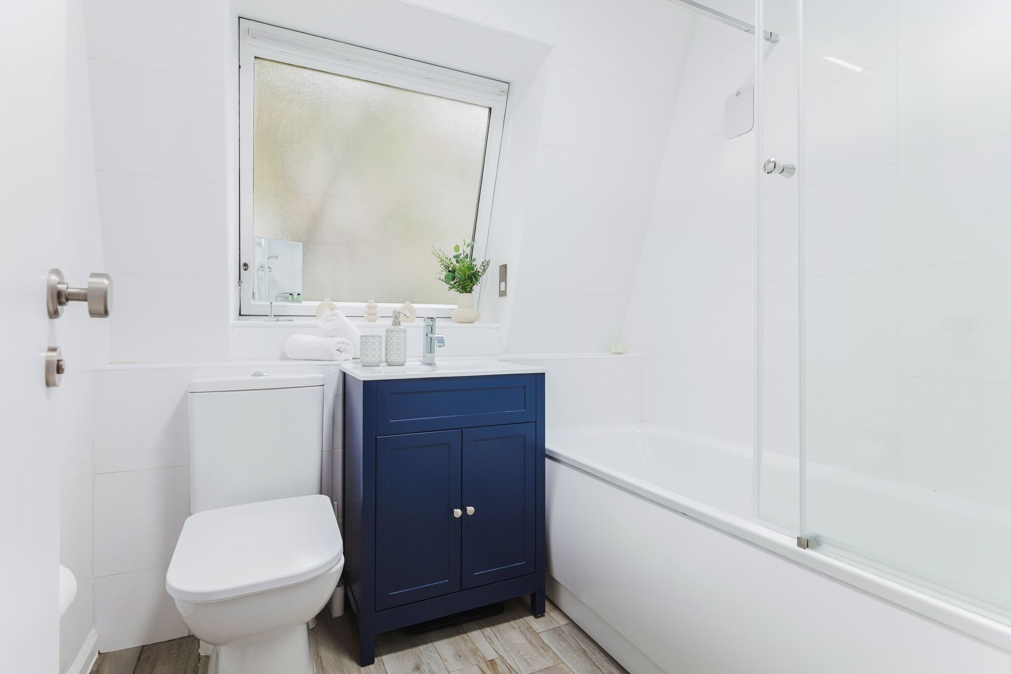 Une petite salle de bain moderne avec des toilettes blanches, un meuble bleu foncé, un lavabo blanc et une douche à parois de verre.