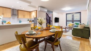A modern kitchen with wooden cabinets, a central island with seating, and a dining area with yellow chairs. - Spacious 2BR House by Madame Tussauds  (London)