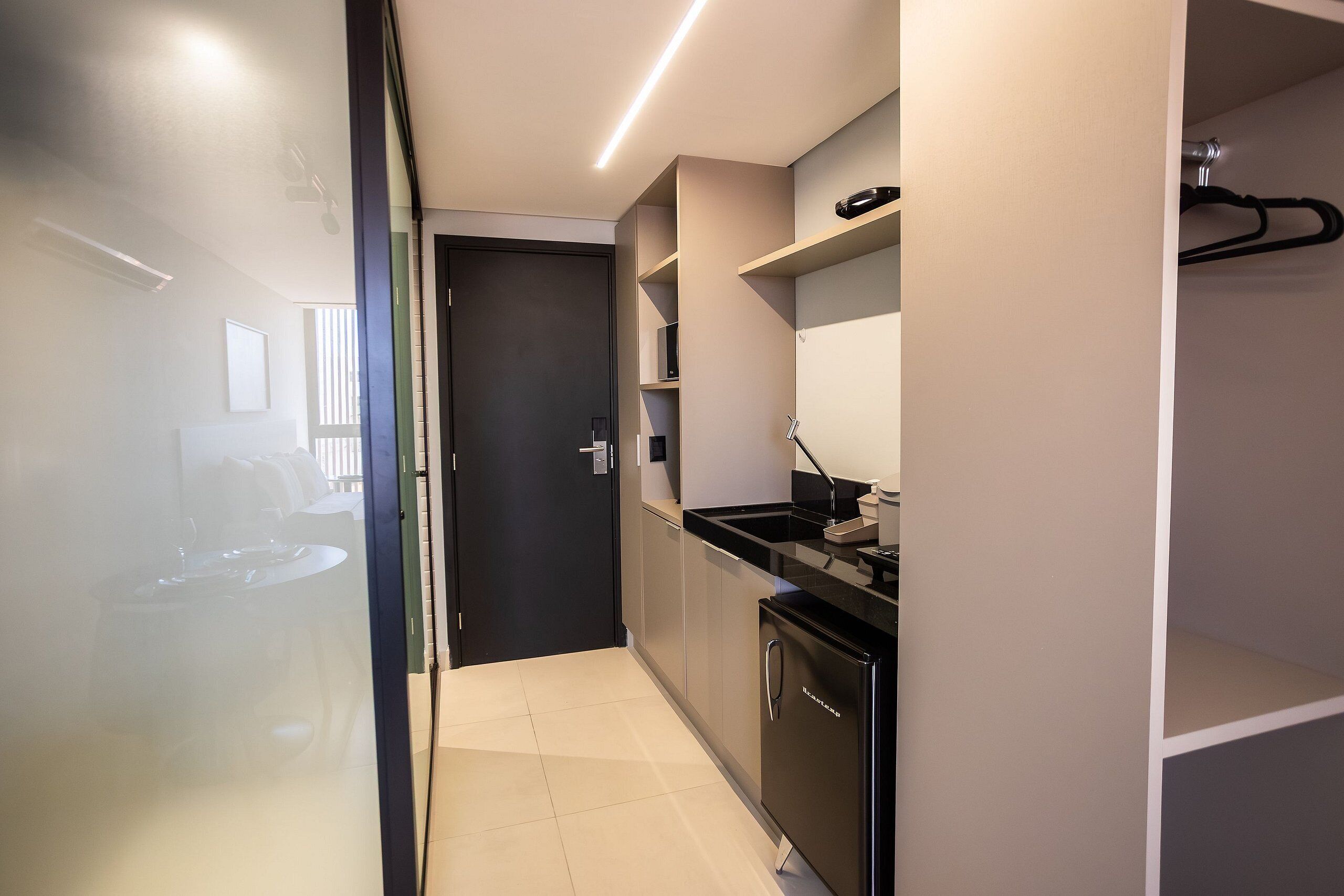 Una cocina moderna con un refrigerador negro, una cafetera y un lavamanos. Hay una puerta que da a otra habitación.
