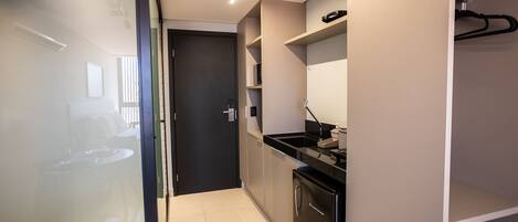 A modern kitchen with a black refrigerator, a coffee machine, and a sink. There is a door leading to another room.