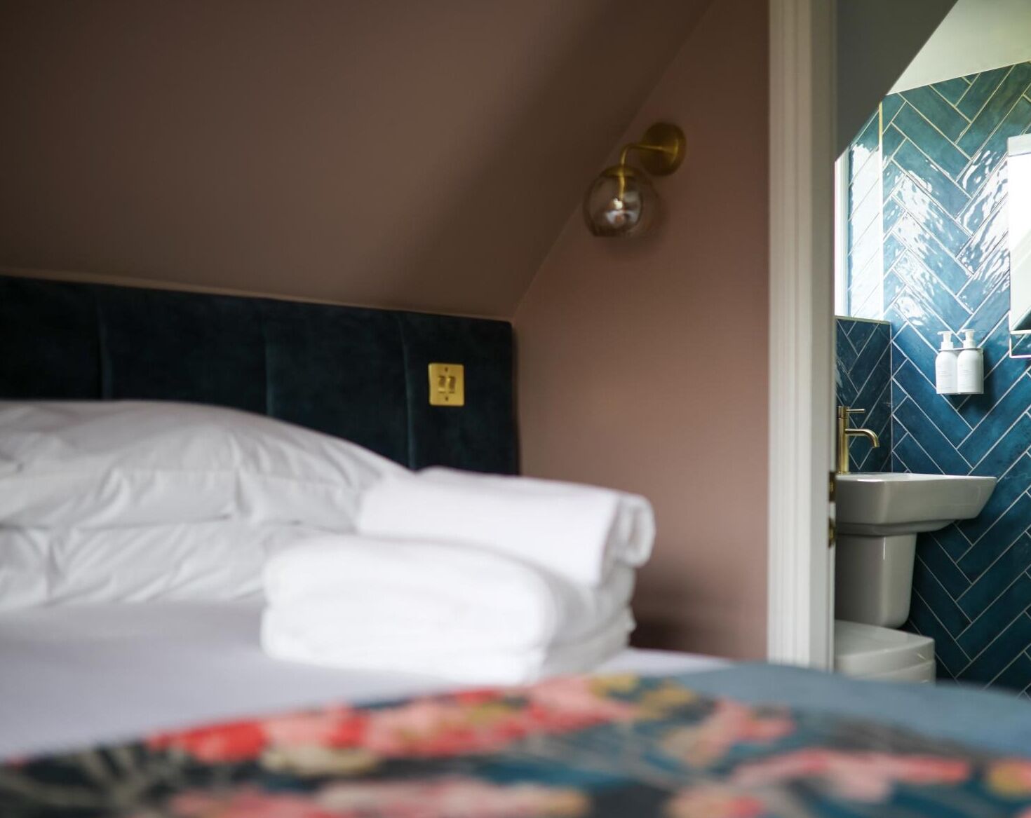 A neatly made bed with white linens, a dark headboard, and a wall-mounted light fixture.