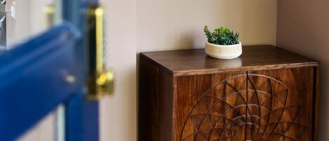 A wooden cabinet with a geometric design, a small plant on top, and a framed picture on the wall.