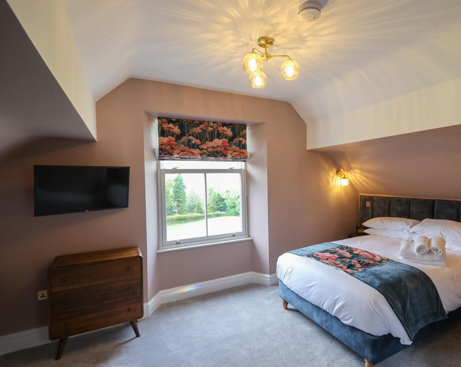 Un dormitorio con cama, cómoda, televisor, ventana con vistas y lámpara de techo.