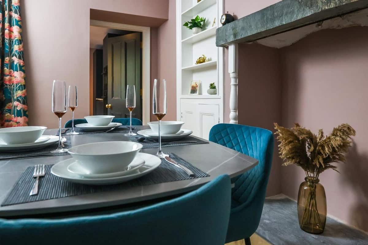 Un coin repas avec une table dressée pour quatre personnes, des chaises et un vase contenant des fleurs séchées.