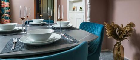 A dining area with a table set for four, chairs, and a vase with dried flowers.