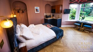A bedroom with a bed, bedside lamps, a small kitchenette, and a window with a view of greenery. - Fair Rigg by Cradel Haus (Windermere)