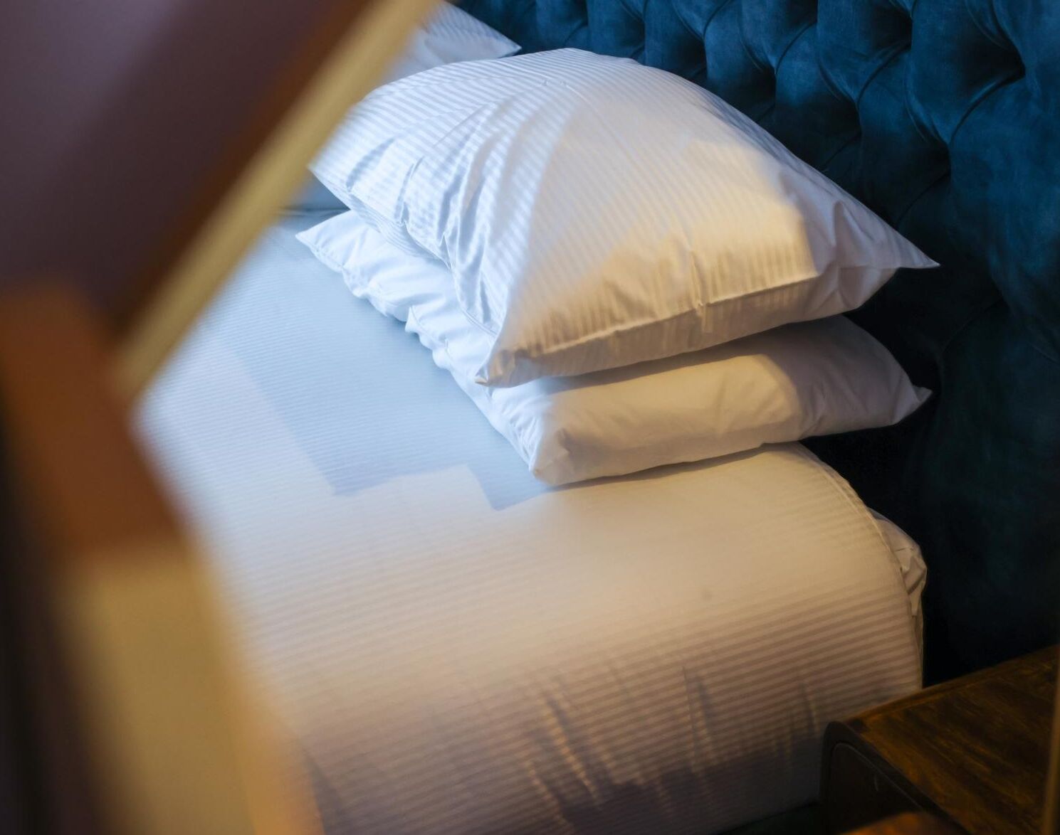 A bed with white linens and a blue upholstered headboard.