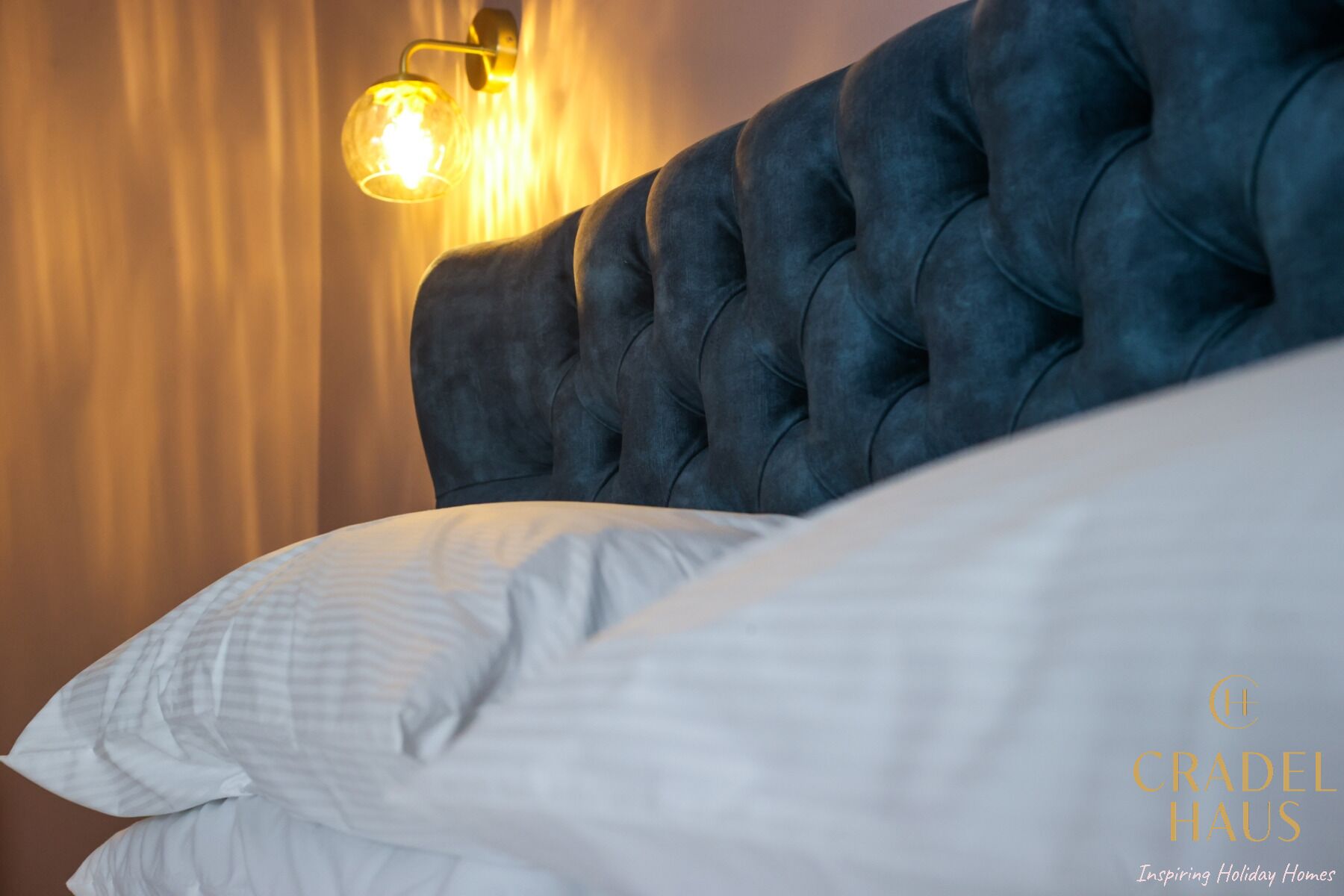 Un dormitorio con cabecera capitonada, lámpara de pared y ropa de cama blanca.
