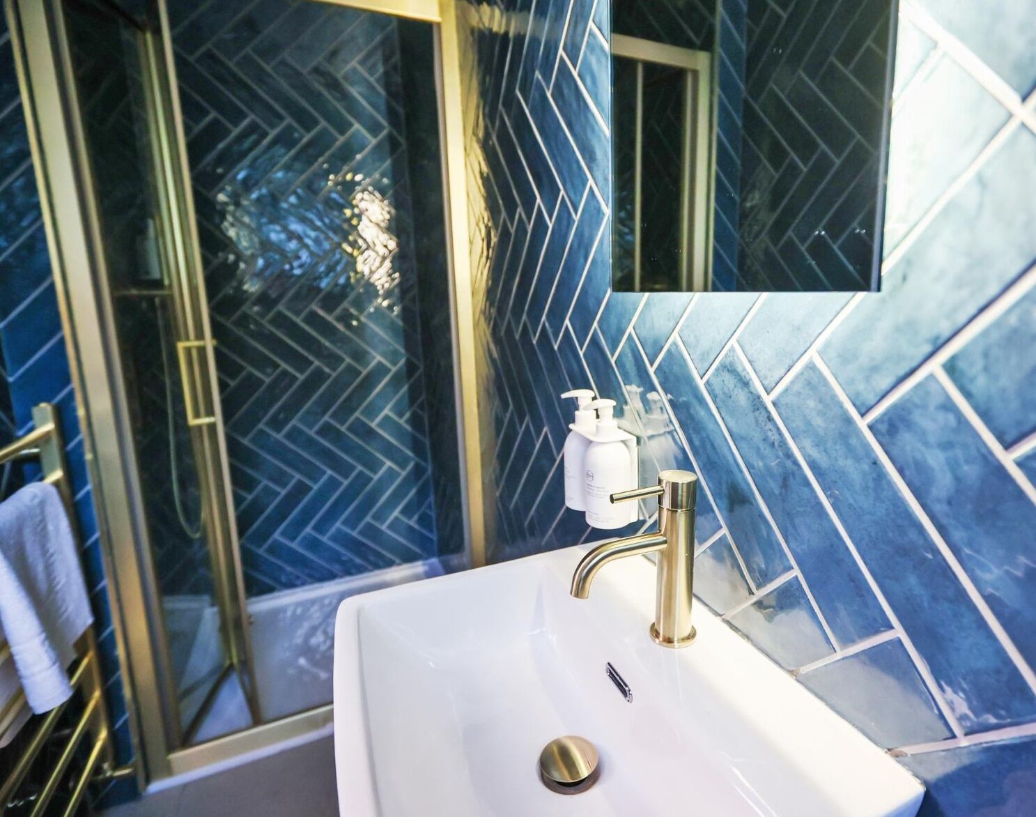 Ein Badezimmer mit einem weißen Waschbecken, einem goldenen Wasserhahn und blauen Fliesen mit Muster.