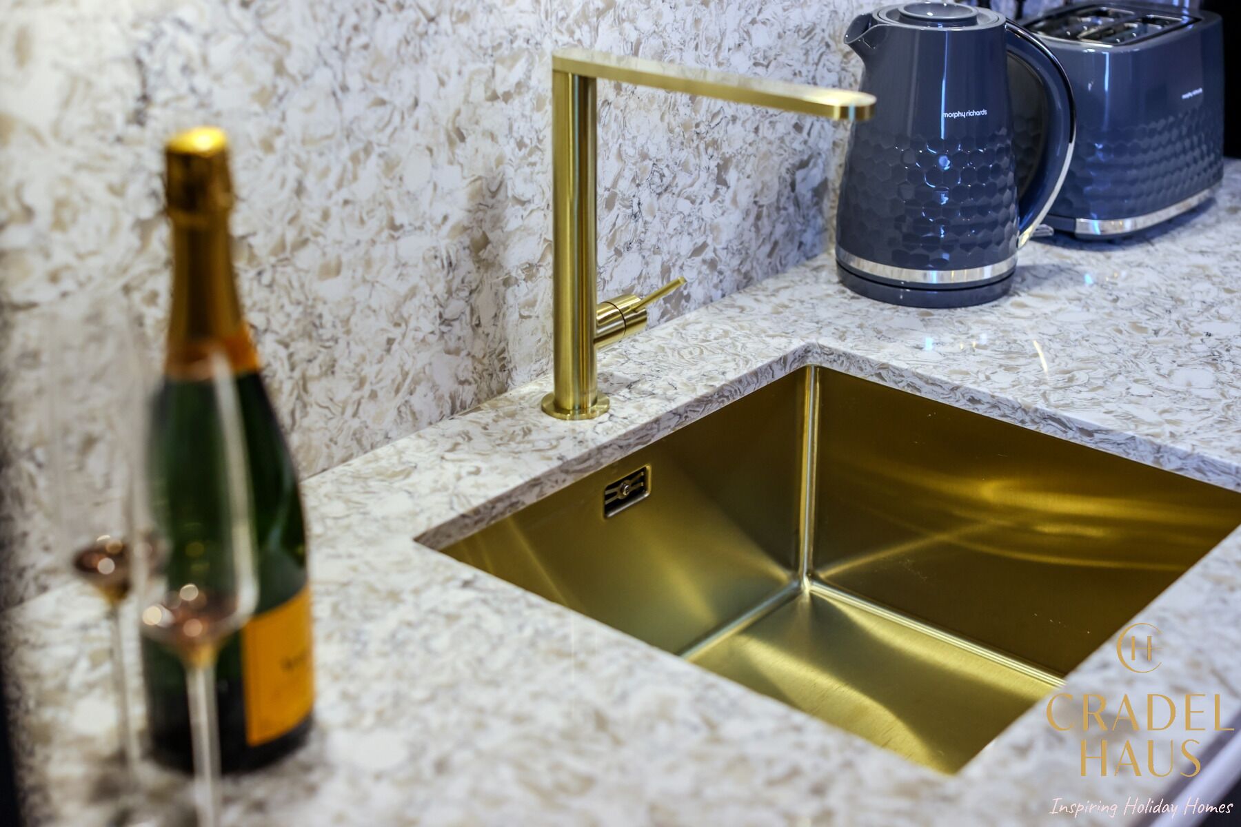 A kitchen with a gold sink, a marble countertop, and a coffee maker.