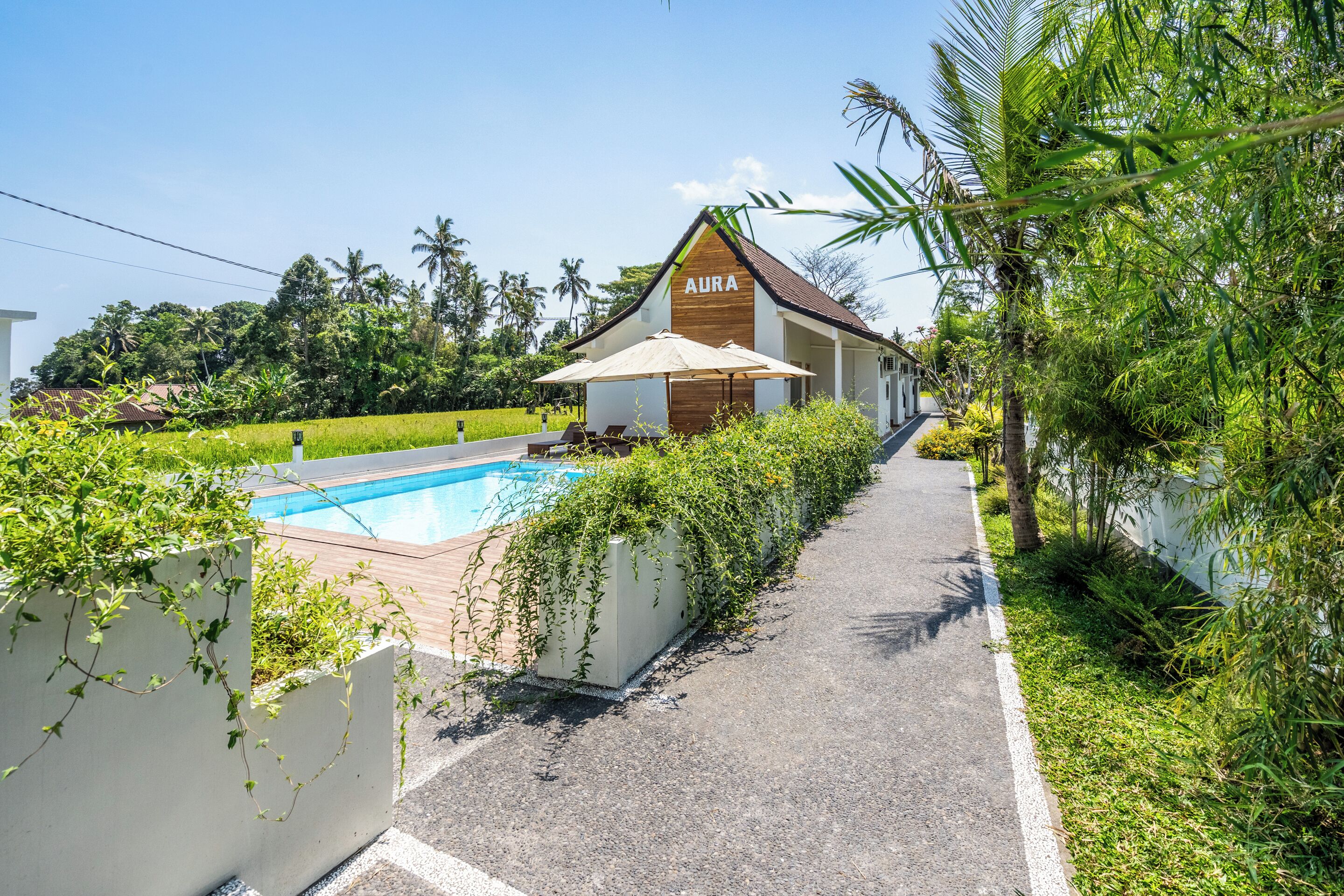 A building labeled "AURA" with a pool, surrounded by lush greenery and palm trees.