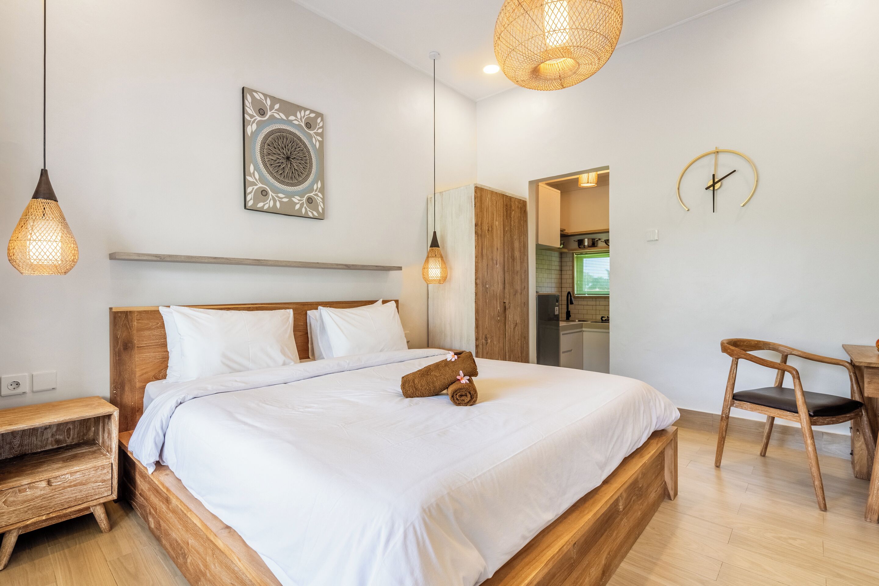 Uma cama bem arrumada com cabeceira de madeira, mesa de cabeceira, relógio de parede e luminária suspensa.