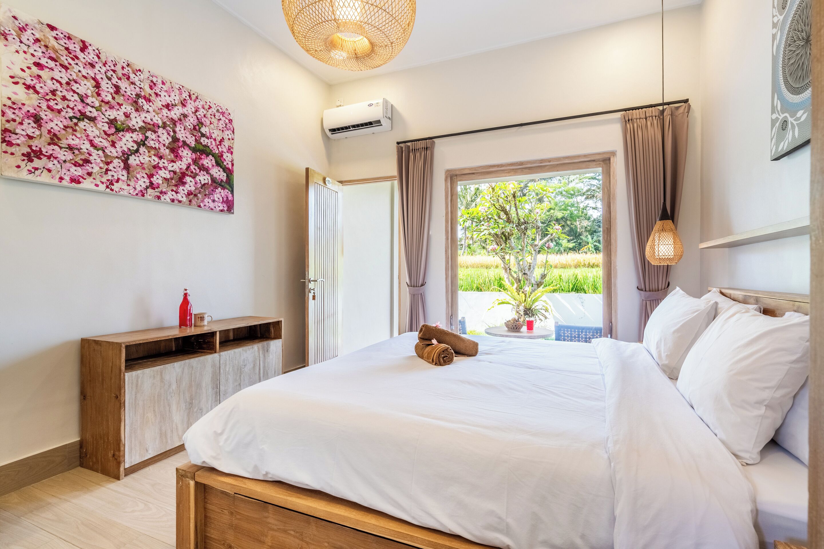 A bedroom with a large bed, a wooden nightstand, a wall-mounted air conditioner, and a window with curtains.