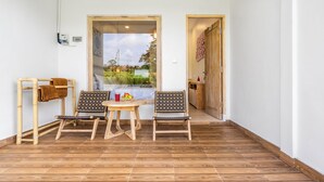 A small room with a wooden floor, two chairs, a table, and a door leading outside. - Aura Apartments Ubud (Ubud)