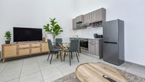 Una cocina moderna con televisión, mesa de comedor, sillas y refrigerador.