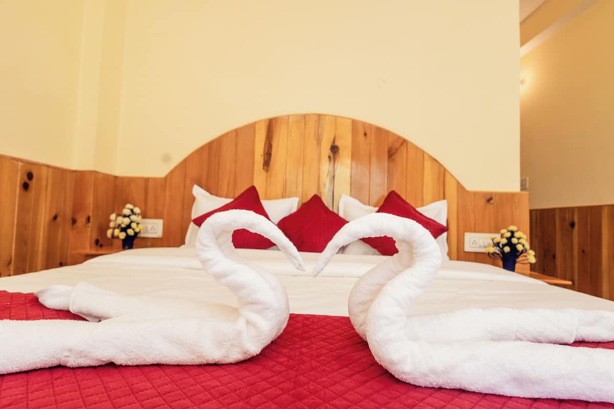 A hotel room with a wooden headboard, red bedding, and two white towels arranged in swan shapes.