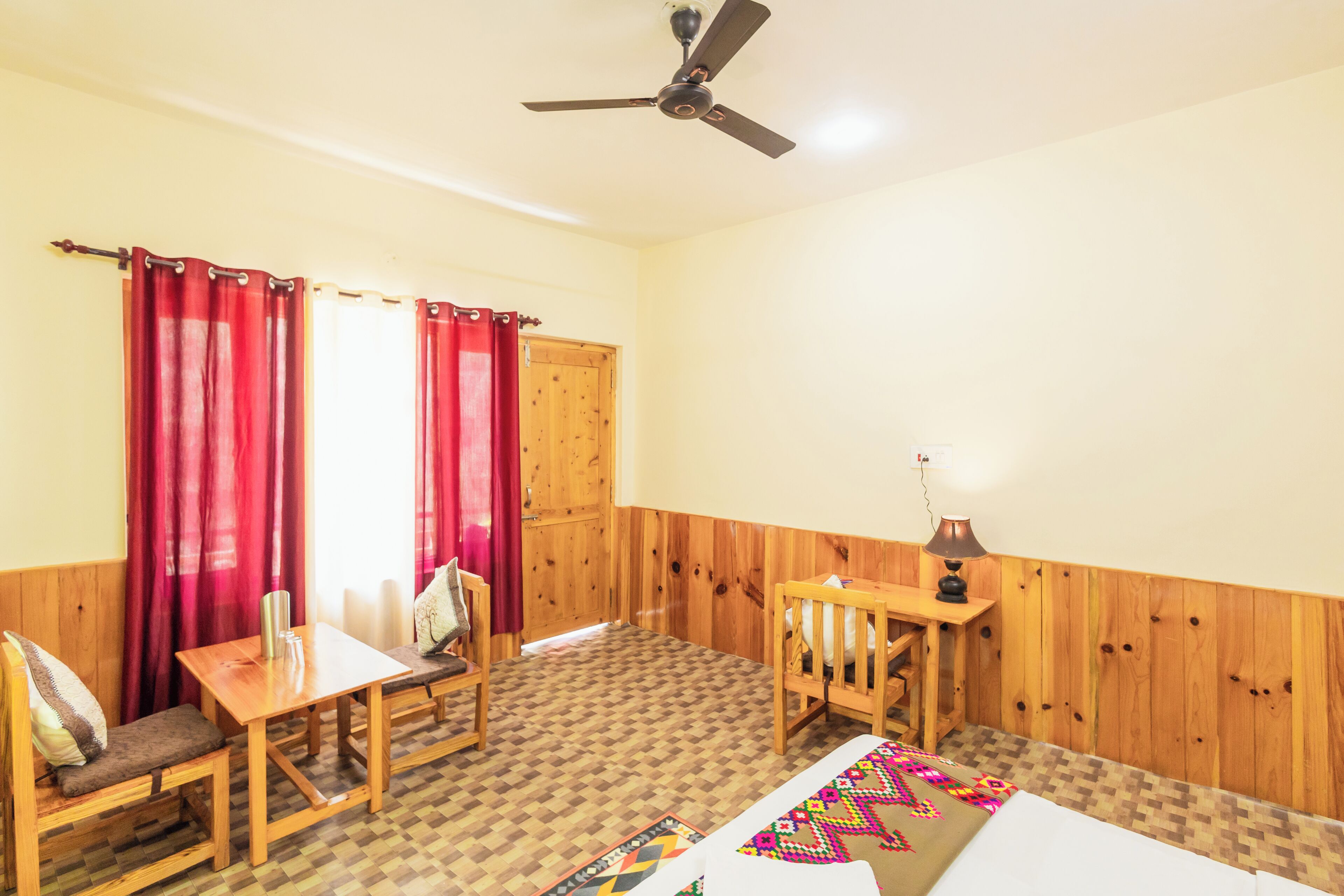 Una habitación con piso de madera, una cama, un escritorio, una silla y un ventilador de techo.