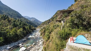 Une rivière traverse une région montagneuse. On aperçoit une tente et une chaise installées sur une petite plateforme en béton.