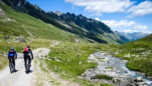 Un sentier de VTT avec deux cyclistes, entouré de collines verdoyantes et traversé par un ruisseau.