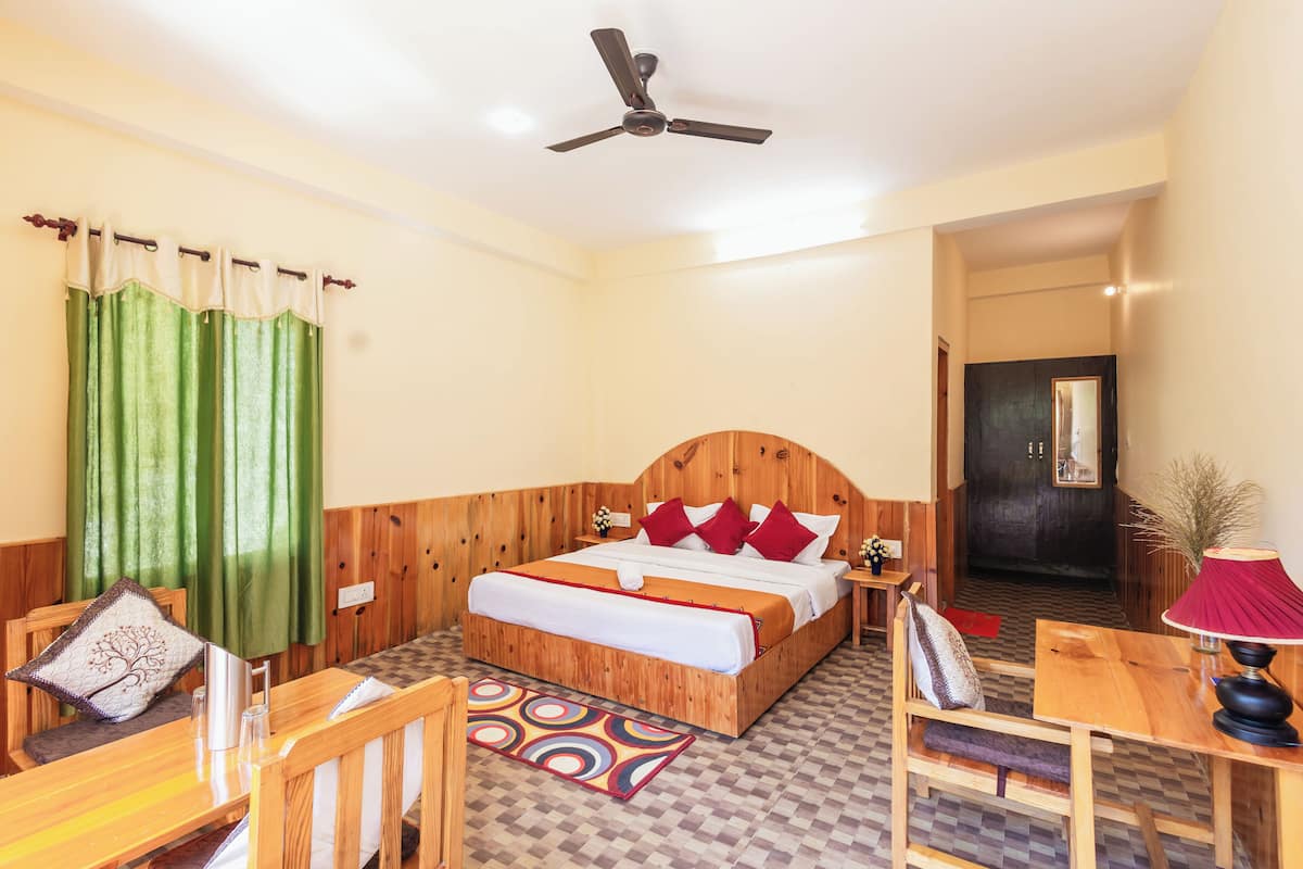 A hotel room with a wooden bed, a desk, a chair, a table, a ceiling fan, and a door.