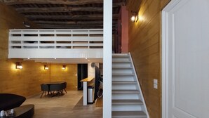 Una habitación estilo loft con comedor, escalera y televisor a la vista.