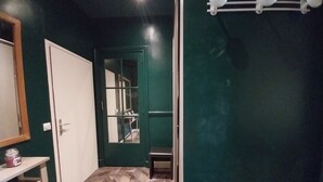 Un pasillo con una puerta verde, una blanca y un espejo a la izquierda.