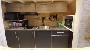 Una cocina compacta con armarios de madera, un microondas, un fregadero y una cafetera.