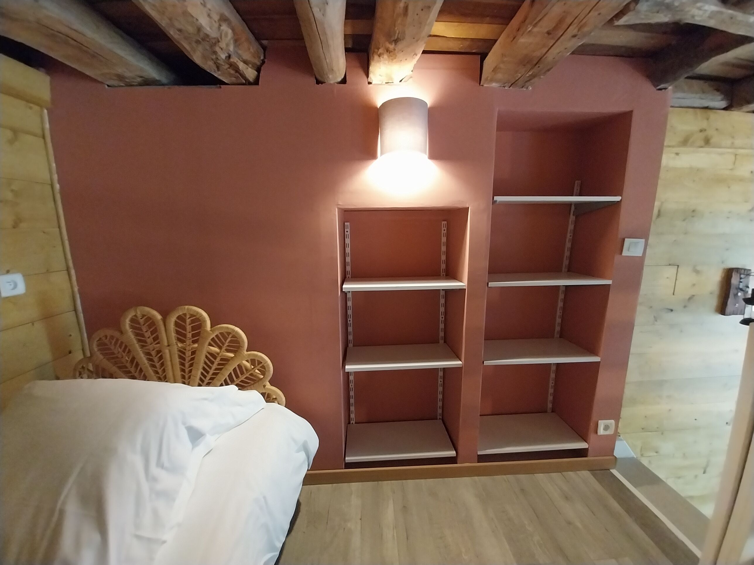 Une chambre avec un lit, une tête de lit en osier et des étagères intégrées.